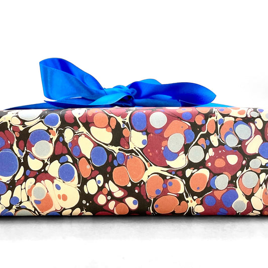 Printed marbled wrapping paper by Jemma Lewis Marbling. Marbled paper in bold red, blue and orange. Pictured wrapped with a blue bow