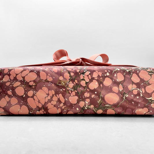 Printed marbled wrapping paper by Jemma Lewis Marbling. Marbled paper in deep burgundy, pinks and brown. Pictured wrapped with a bow