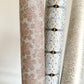 Japanese silkscreen chiyogami paper with a repeat pattern of cherry blossom flowers in taupe and white, pictured rolled with other designs