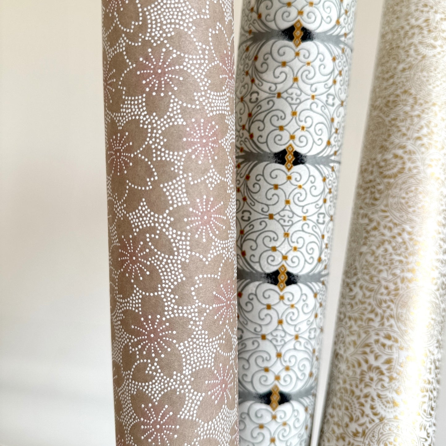 Japanese silkscreen chiyogami paper with a repeat pattern of cherry blossom flowers in taupe and white, pictured rolled with other designs