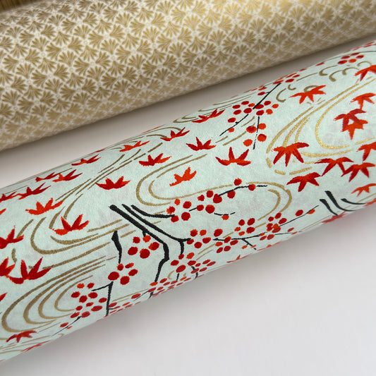 a sheet of japanese silkscreen printed chiyogami paper with a pattern of gold rivers, red falling leaves on a soft aqua background. close up