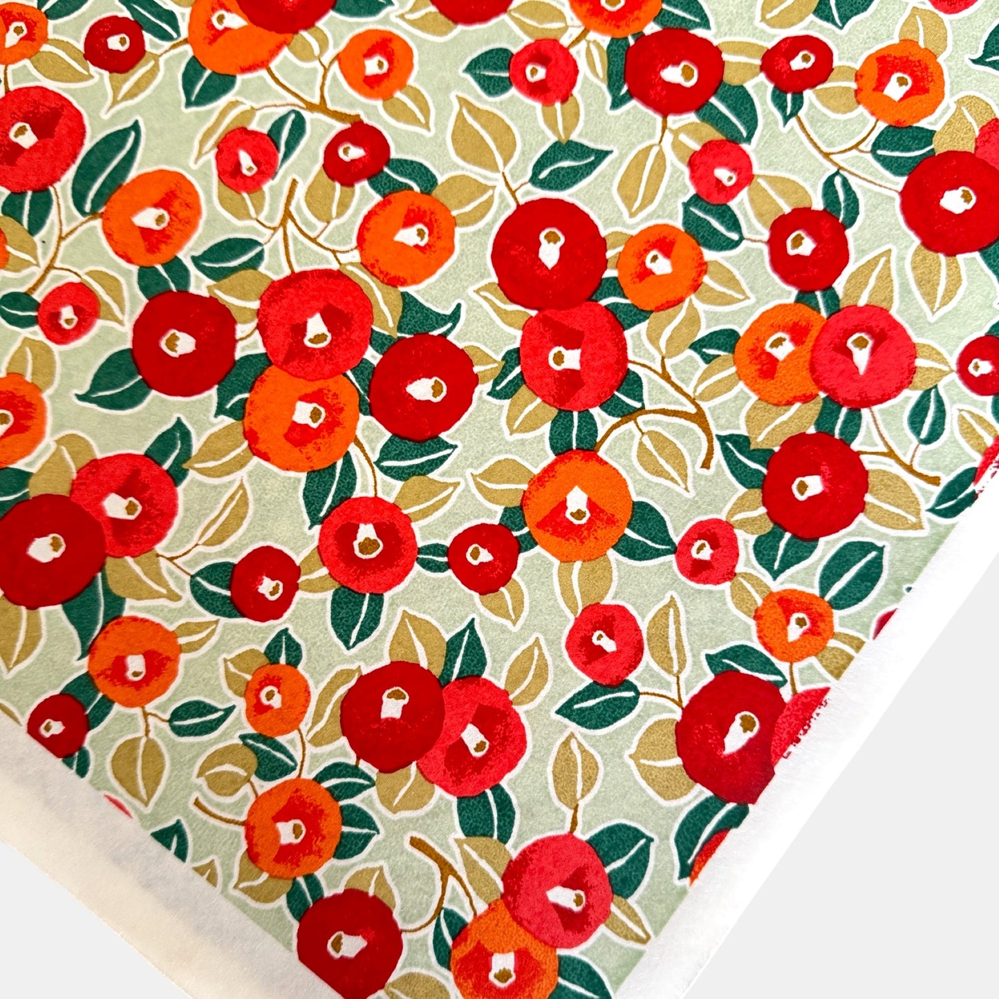 Japanese silkscreen chiyogami paper with a repeat pattern of camellia flowers in red and orange on a soft green ground