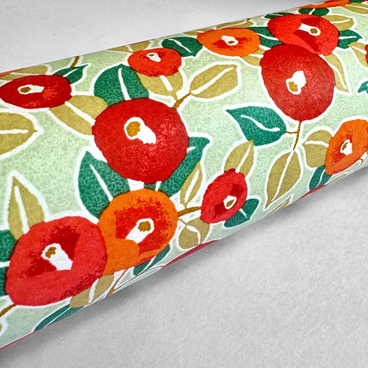 Japanese silkscreen chiyogami paper with a repeat pattern of camellia flowers in red and orange on a soft green ground. Close up