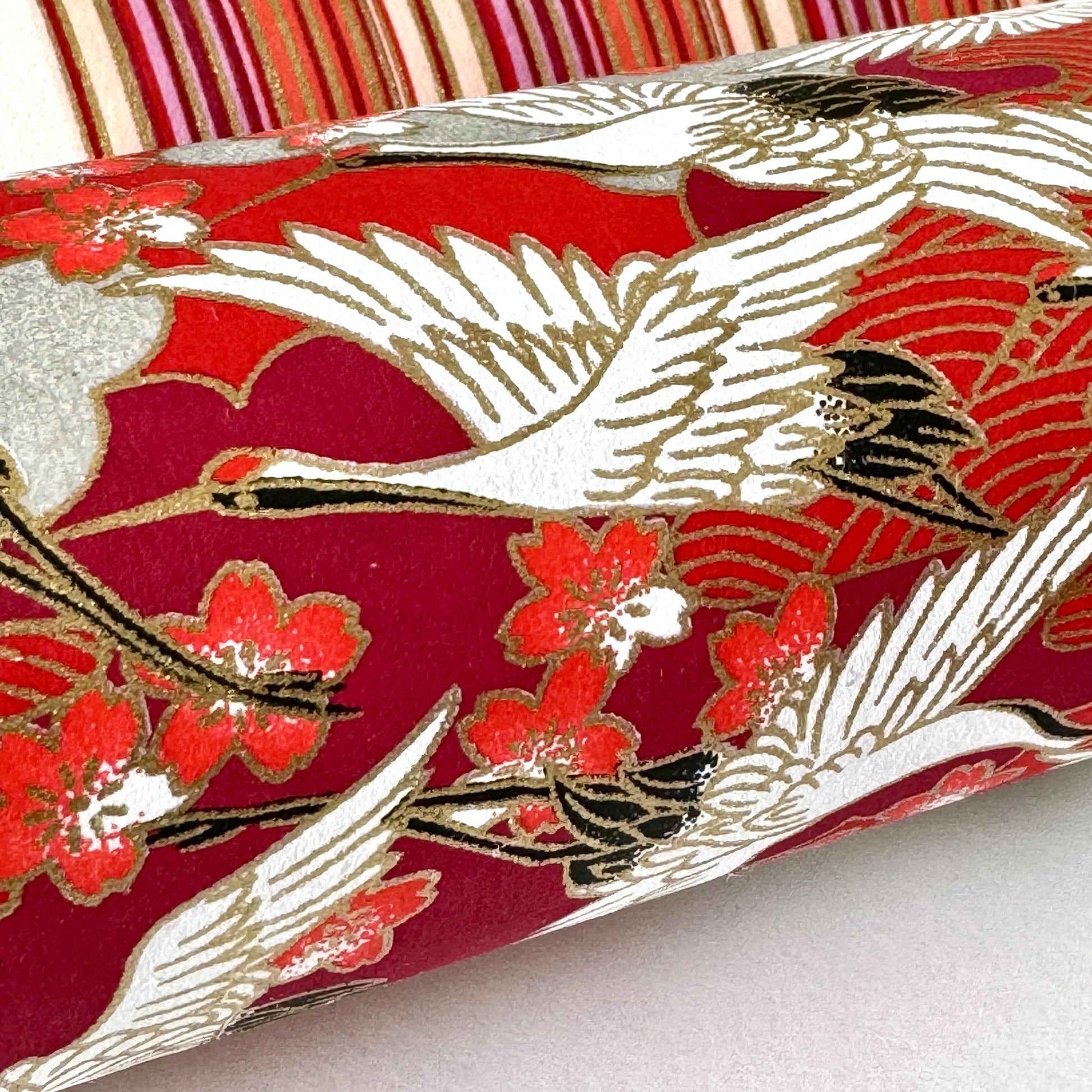 Japanese silkscreen chiyogami paper with a repeat pattern of white cranes in flight on a red and silver background, close up