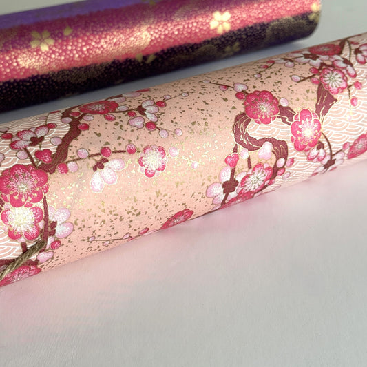Diagonal branches of pink plum (ume) blossom on a light pink background with gold accents. Japanese chiyogami paper