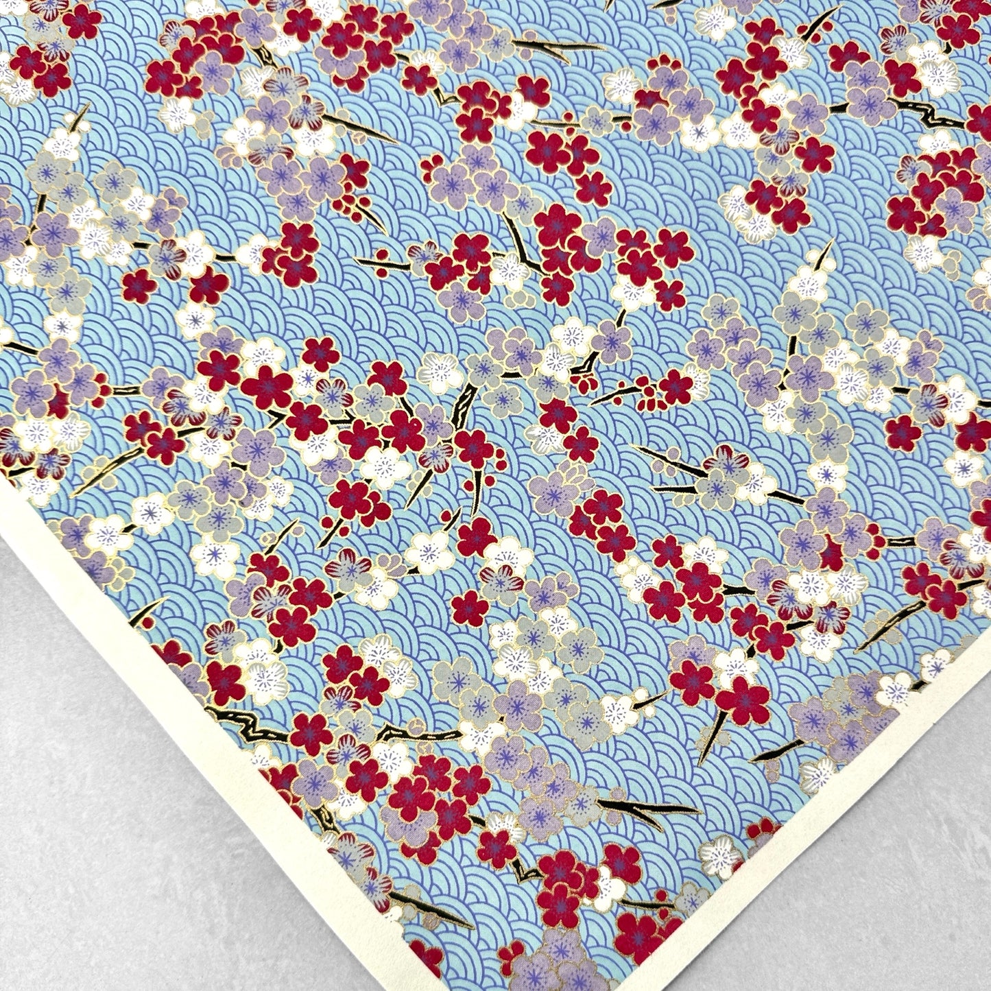 Japanese silkscreen chiyogami paper with a pattern of deep red, lilac and white plum blossom on a blue backdrop