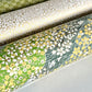Japanese silkscreen chiyogami paper with a pattern of dark green rivers and grass green banks with an abundance of little flowers in white and yellow. Close up