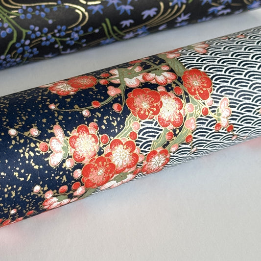 Diagonal branches of rich pink plum (ume) blossom on a midnight blue background with gold accents. Japanese chiyogami paper
