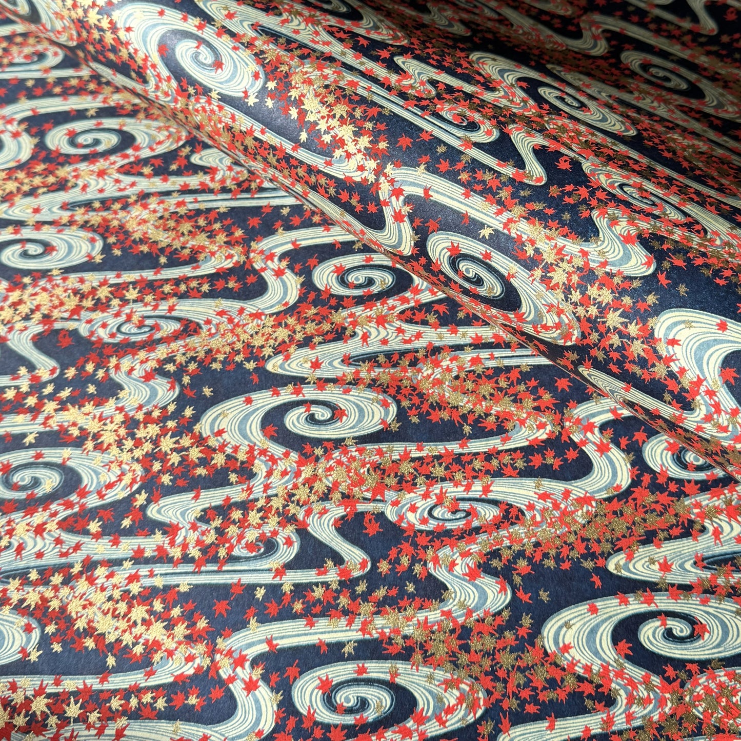a sheet of Japanese chiyogami paper with a pattern of swirling streams with red and gold falling leaves, dark blue background