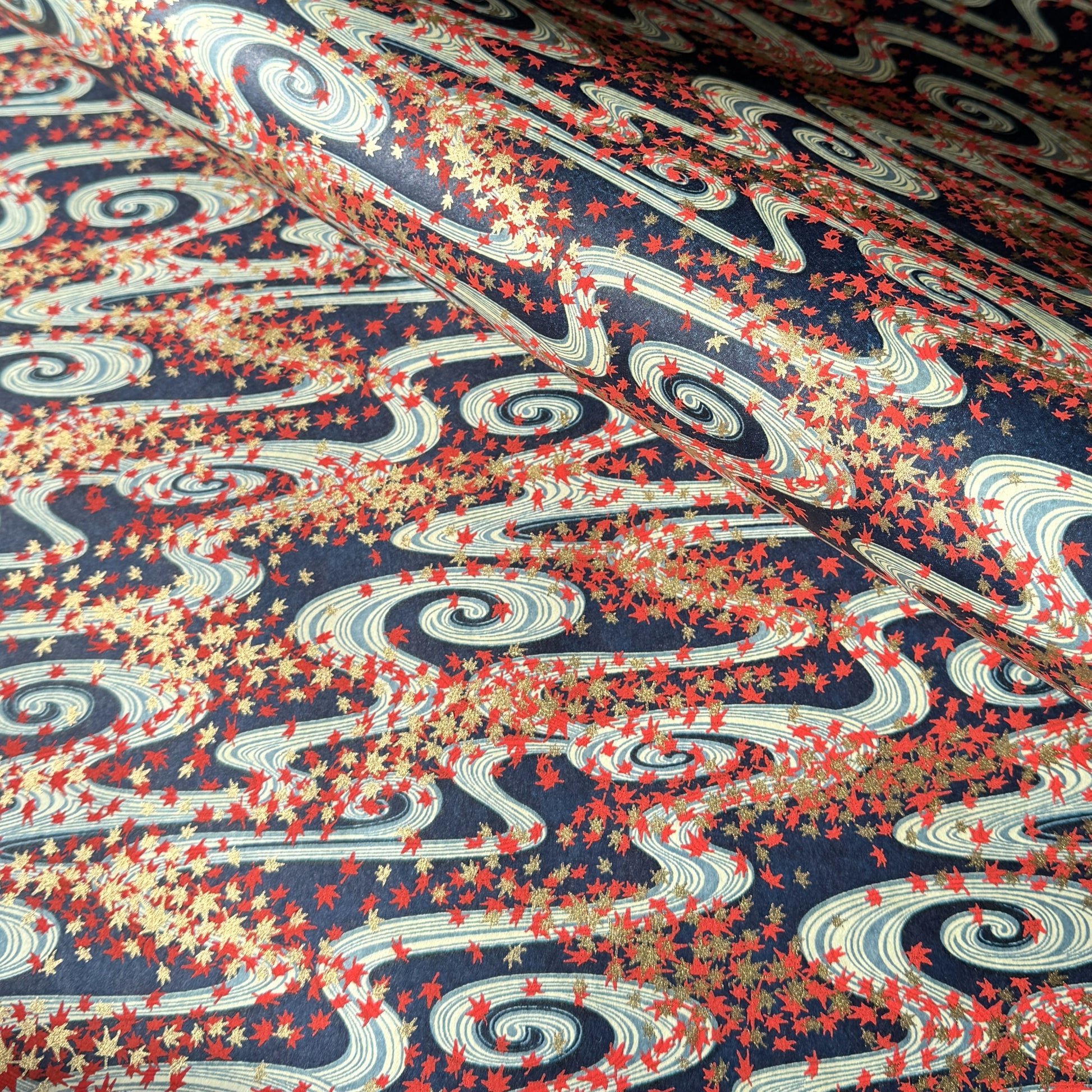 a sheet of Japanese chiyogami paper with a pattern of swirling streams with red and gold falling leaves, dark blue background
