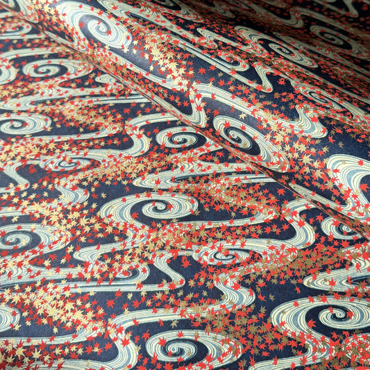a sheet of Japanese chiyogami paper with a pattern of swirling streams with red and gold falling leaves, dark blue background