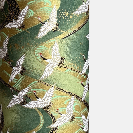 a sheet of Japanese chiyogami paper with white cranes flying on a dark green and gold swirl background