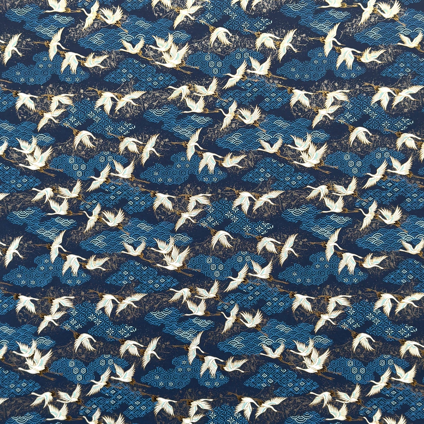 a sheet of Japanese chiyogami yuzen paper with a traditional pattern of white cranes flying with a deep blue background of patterned clouds