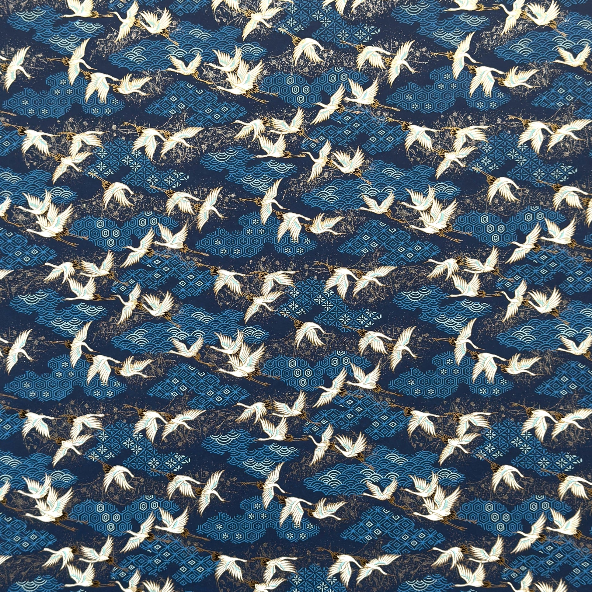 a sheet of Japanese chiyogami yuzen paper with a traditional pattern of white cranes flying with a deep blue background of patterned clouds