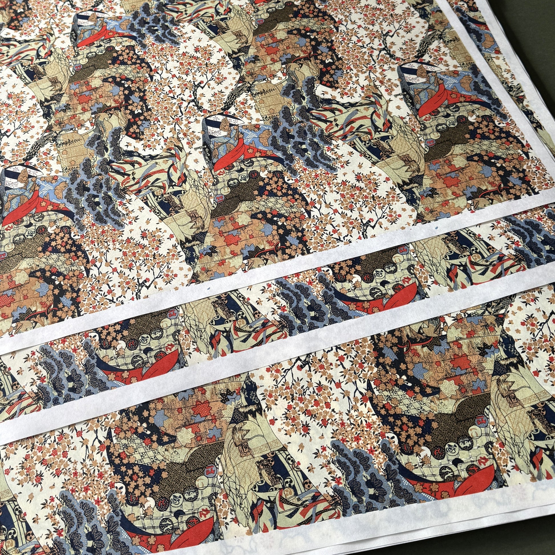 A sheet of Chiyogami paper with a traditional Japanese pattern of a detailed hillside in blue, red, bronze and black. 