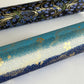 japanese chiyogami paper in stripes of blue, turquoise and grey with gold clouds and flowers. close up rolled