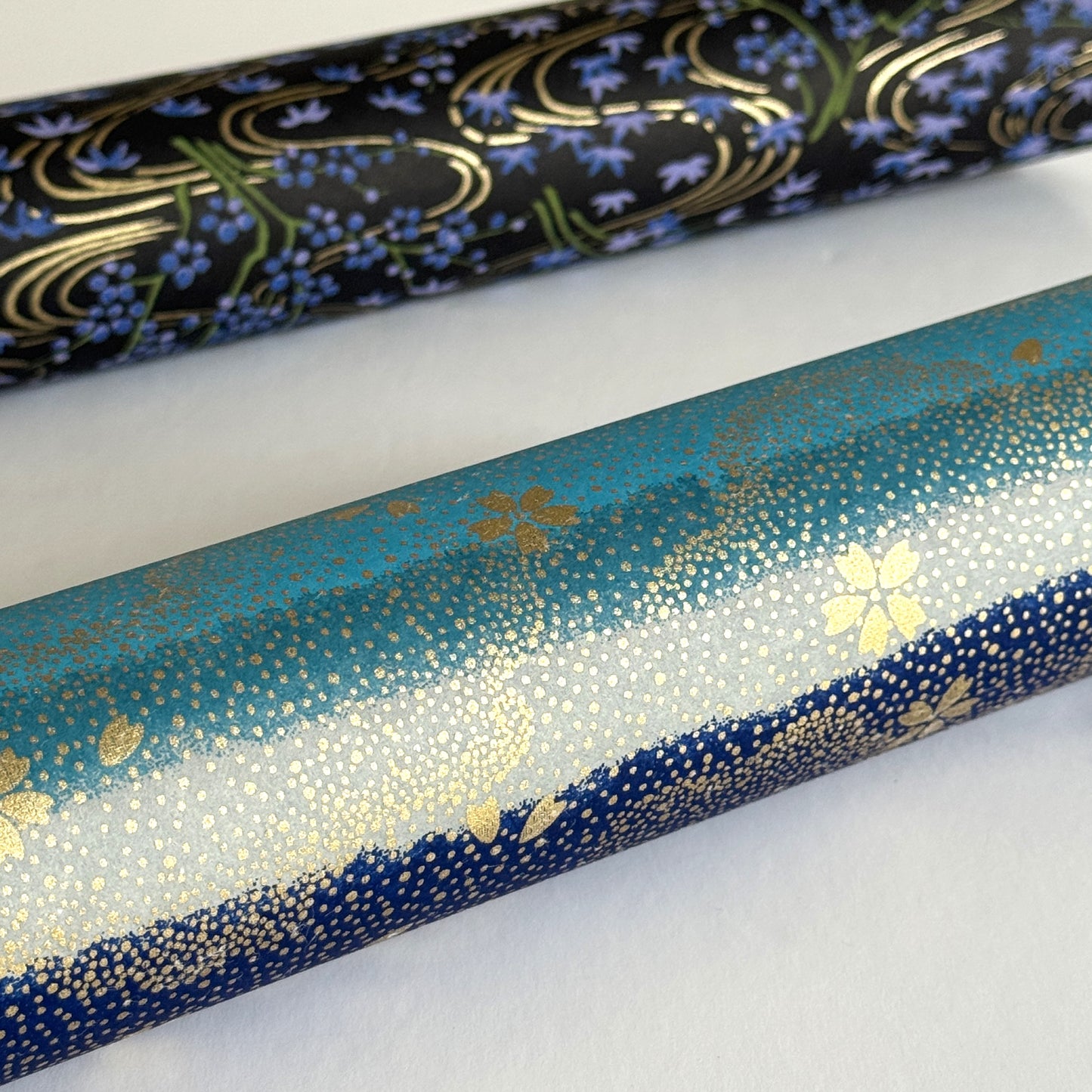japanese chiyogami paper in stripes of blue, turquoise and grey with gold clouds and flowers. close up rolled