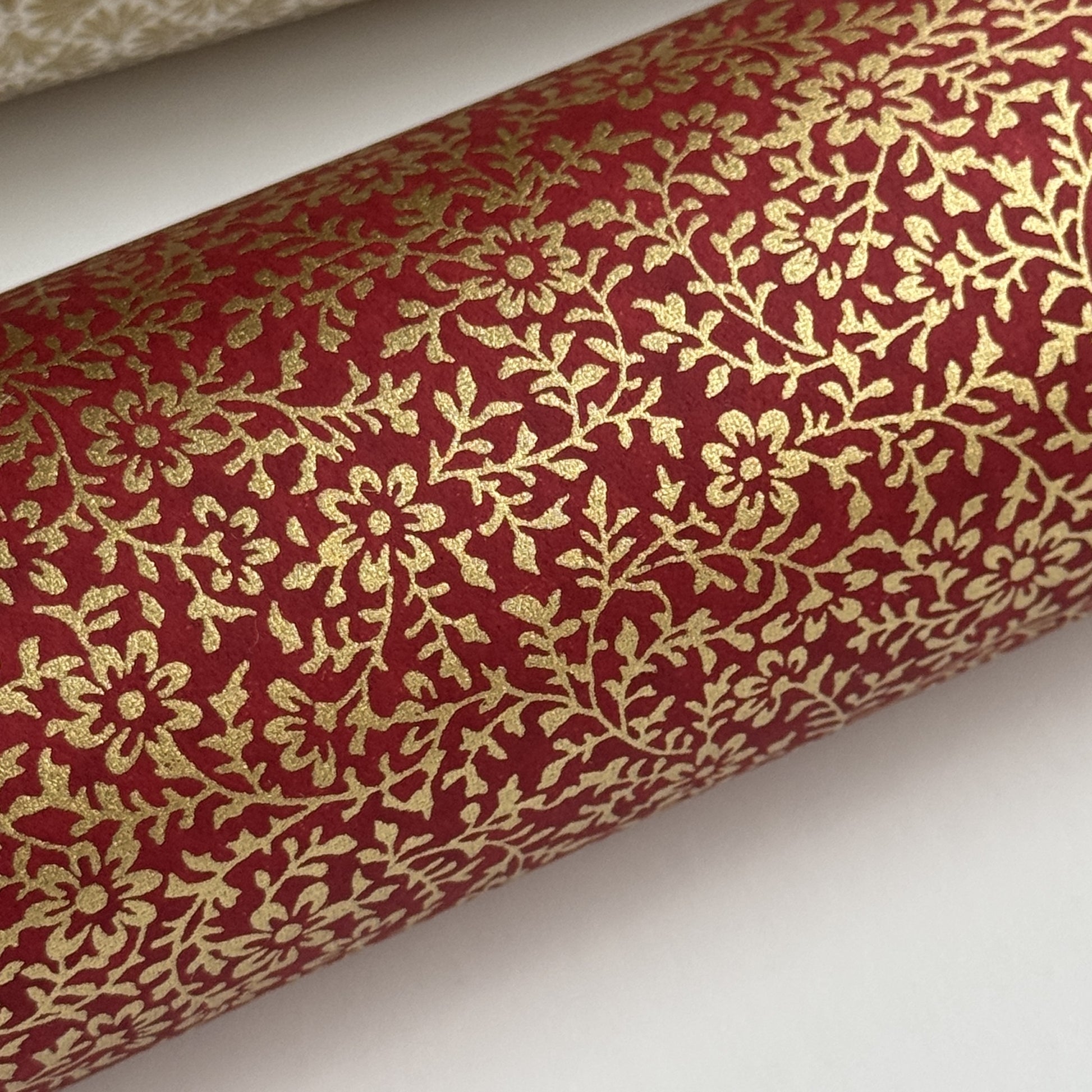 a sheet of Japanese chiyogami yuzen paper with a ditsy gold floral design on a deep red. close up