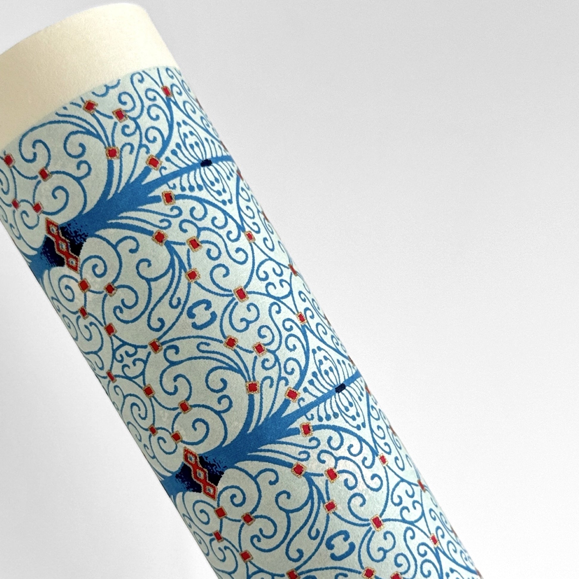 Japanese silkscreen chiyogami paper with a intricate filigree trellis design in blue with red and gold accent. Pictured rolled