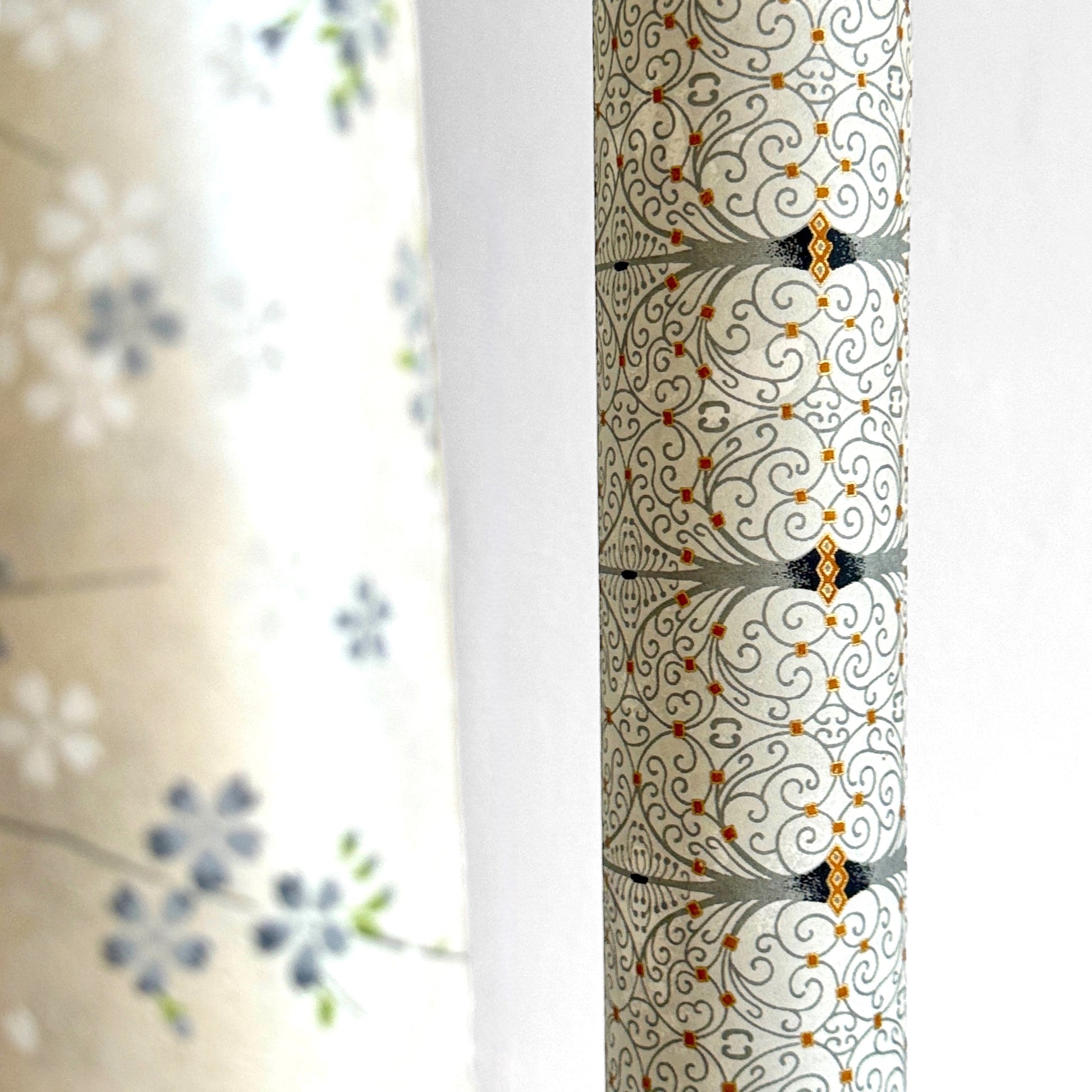 Japanese silkscreen chiyogami paper with a intricate filigree trellis design in grey with gold accent. Pictured rolled