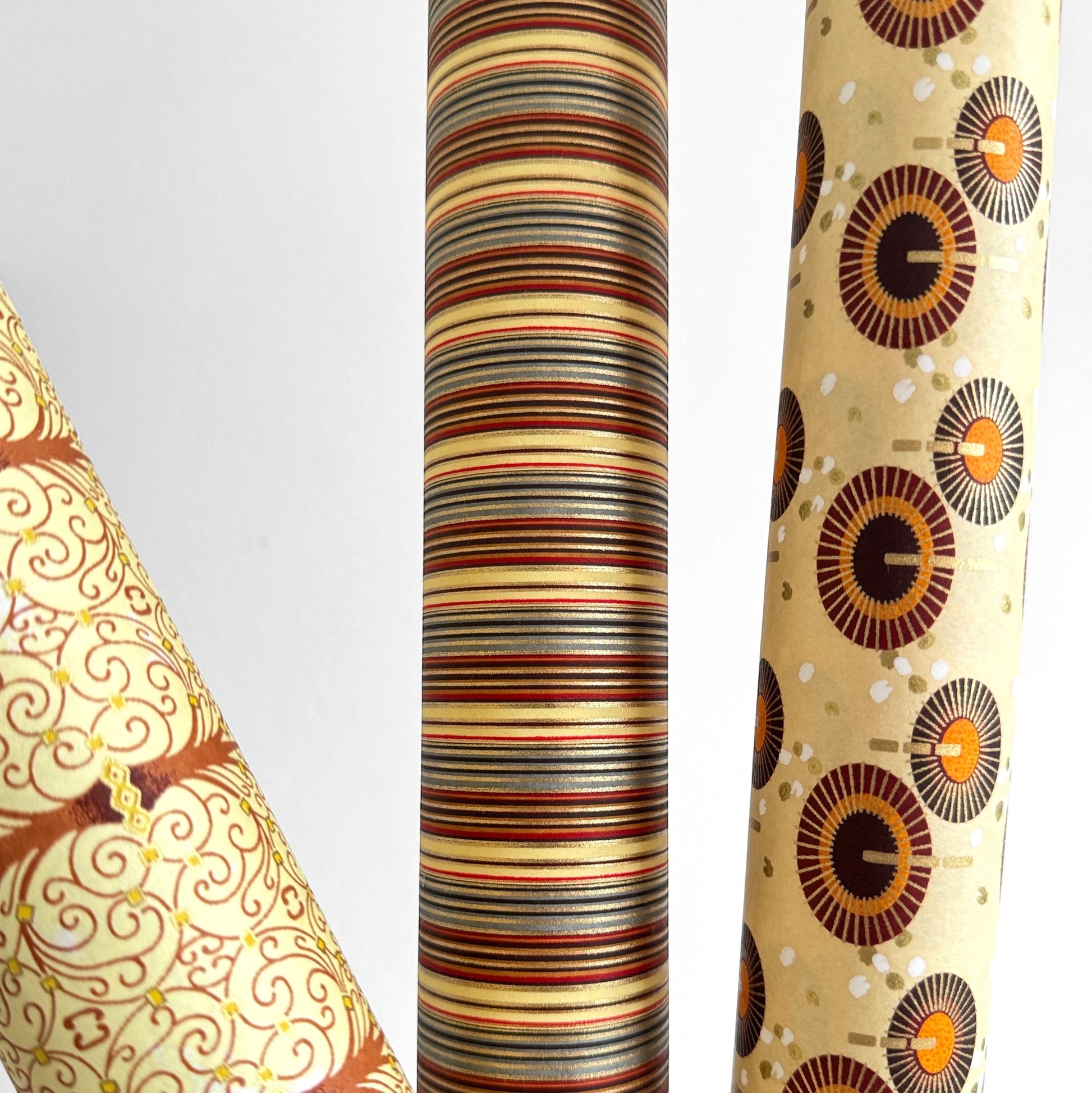 Japanese silkscreen chiyogami paper with a classic narrow stripe pattern in earthy tones of brown, grey, cream, black and gold. Pictured rolled with other designs.