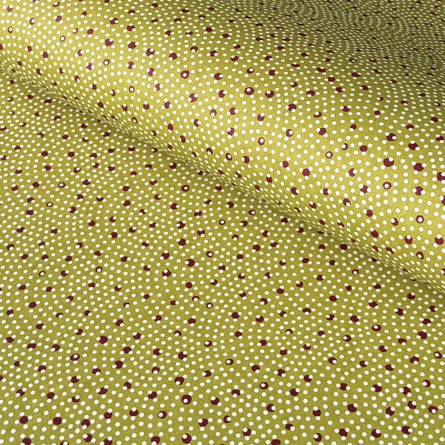 a sheet of Japanese chiyogami paper with an olive backdrop and a white dotted repeat arch pattern with red dots