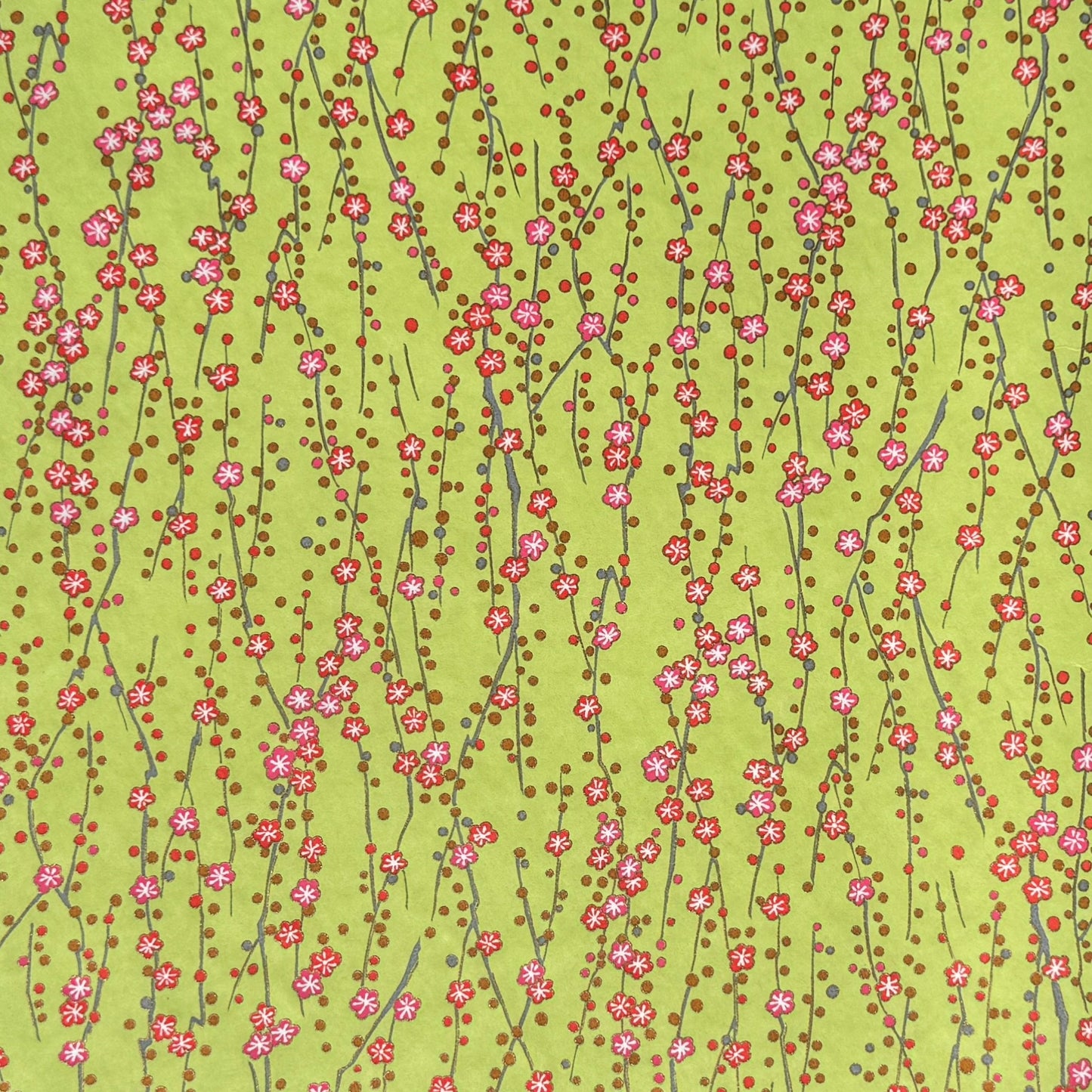 a sheet of chiyogami paper with a lime green background and vertical pattern of little plum flower trails in pink and gold