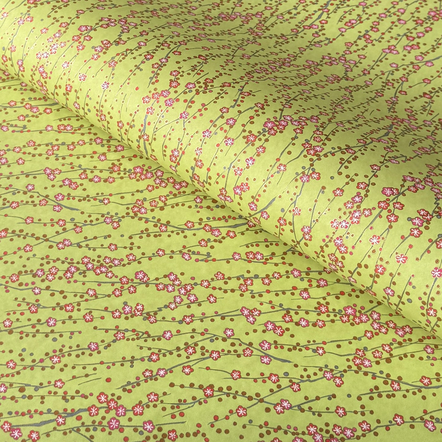 a sheet of chiyogami paper with a lime green background and vertical pattern of little plum flower trails in pink and gold