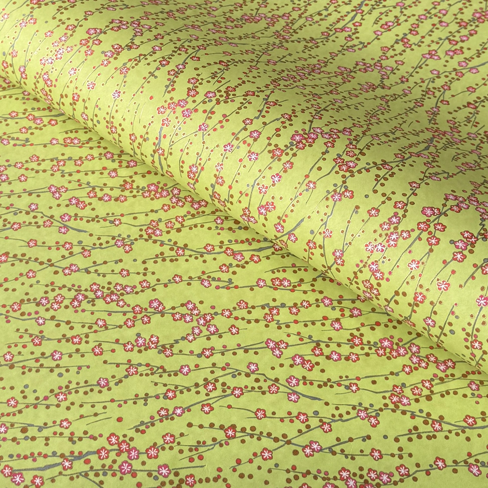 a sheet of chiyogami paper with a lime green background and vertical pattern of little plum flower trails in pink and gold
