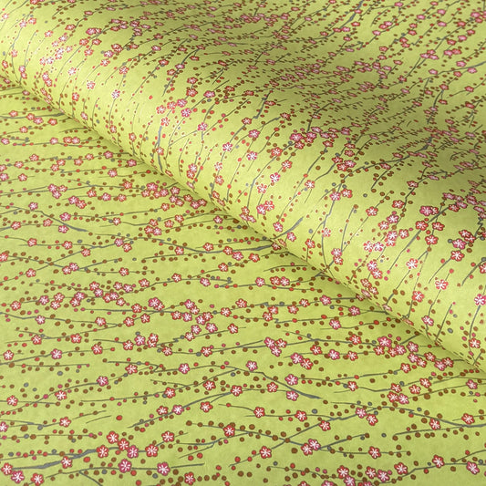 a sheet of chiyogami paper with a lime green background and vertical pattern of little plum flower trails in pink and gold