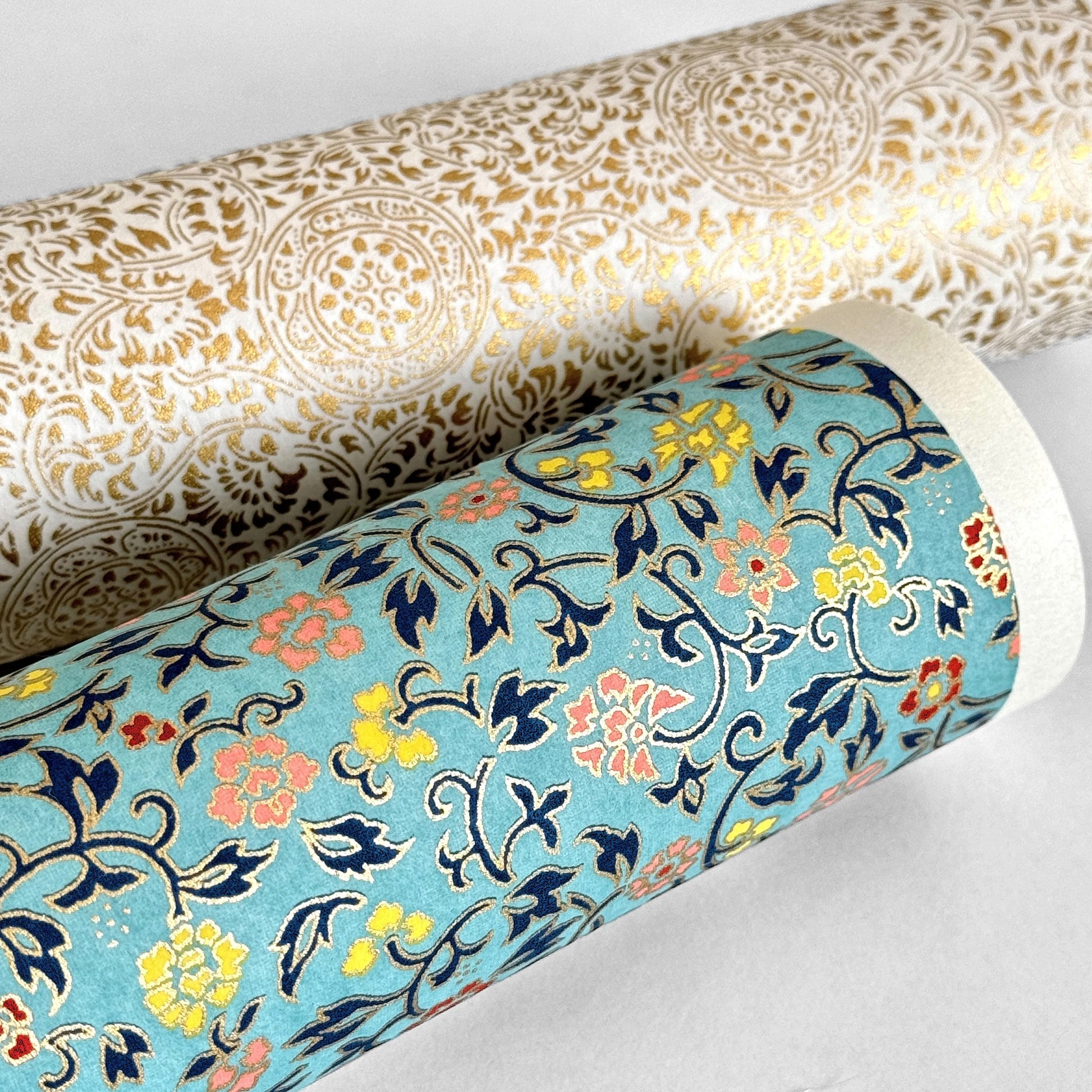 Japanese silkscreen chiyogami paper with a dainty floral pattern in navy, yellow and coral on a teal backdrop. Finished with gold metallic ink. Pictured rolled