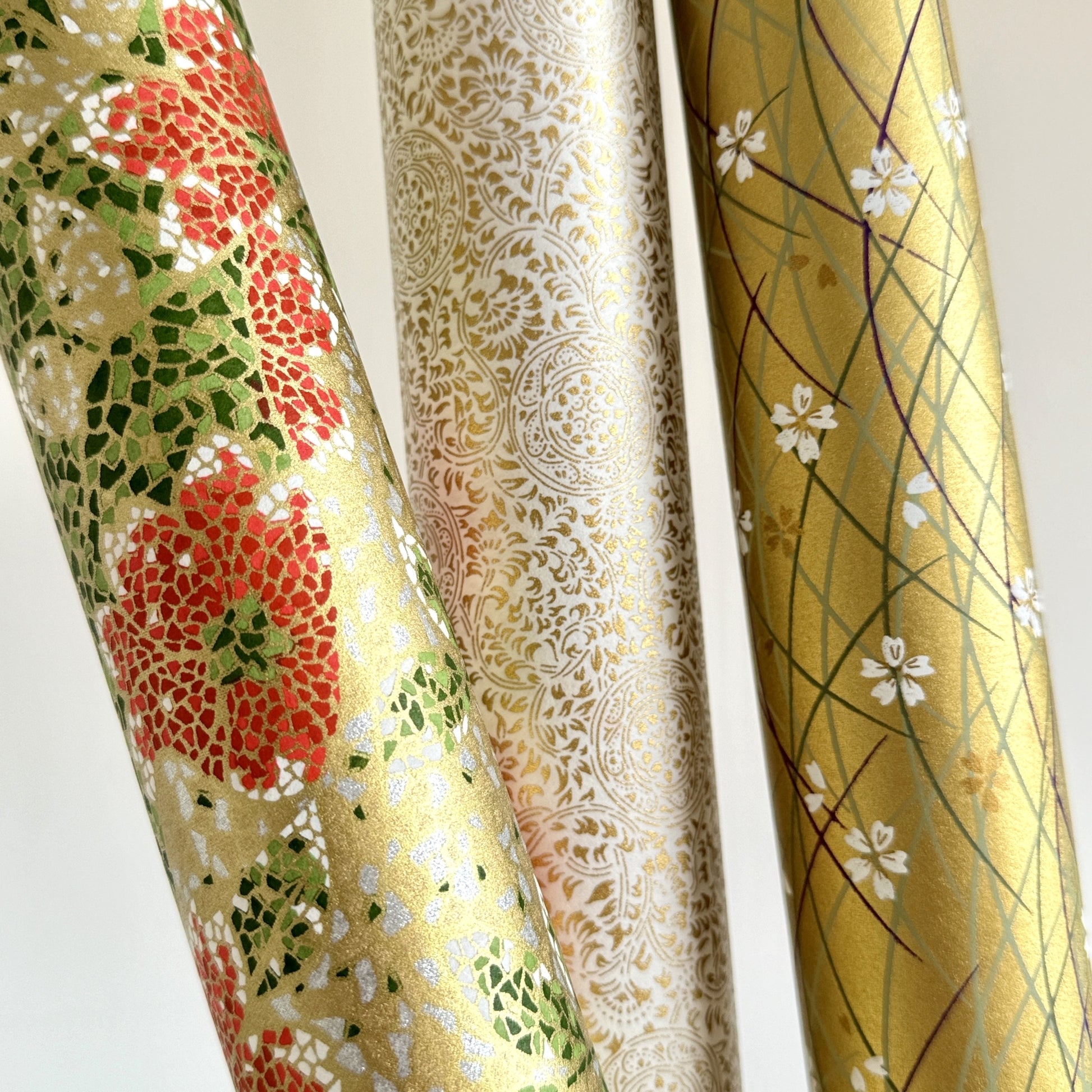 Japanese silkscreen chiyogami paper with a mosaic pattern of scarlet chrysanthemums on gold with green foliage. Pictured rolled with other designs.
