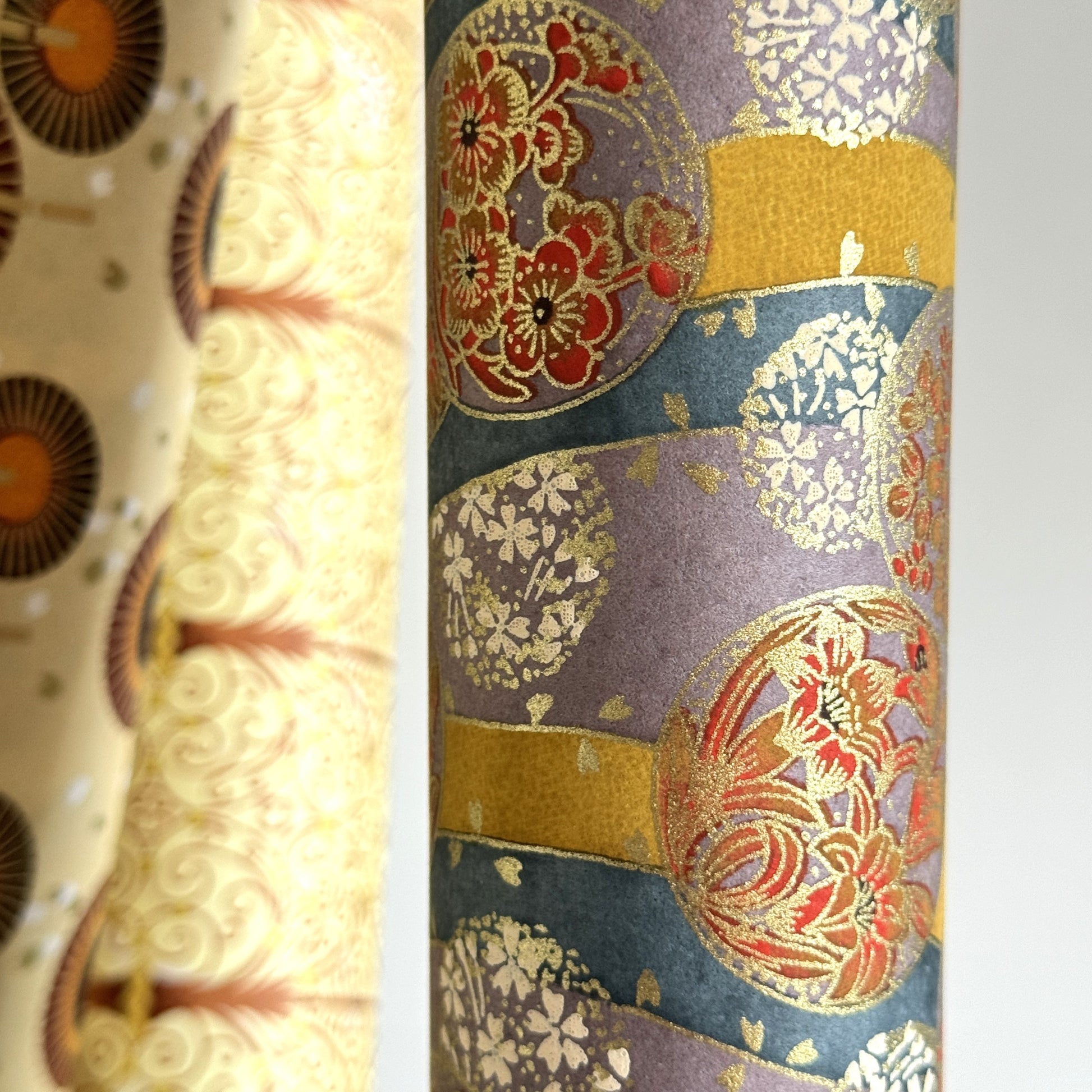 Japanese silkscreen chiyogami paper with a traditional botanical circle motif in tones of mustard, inky blue, lilac and gold. Close up
