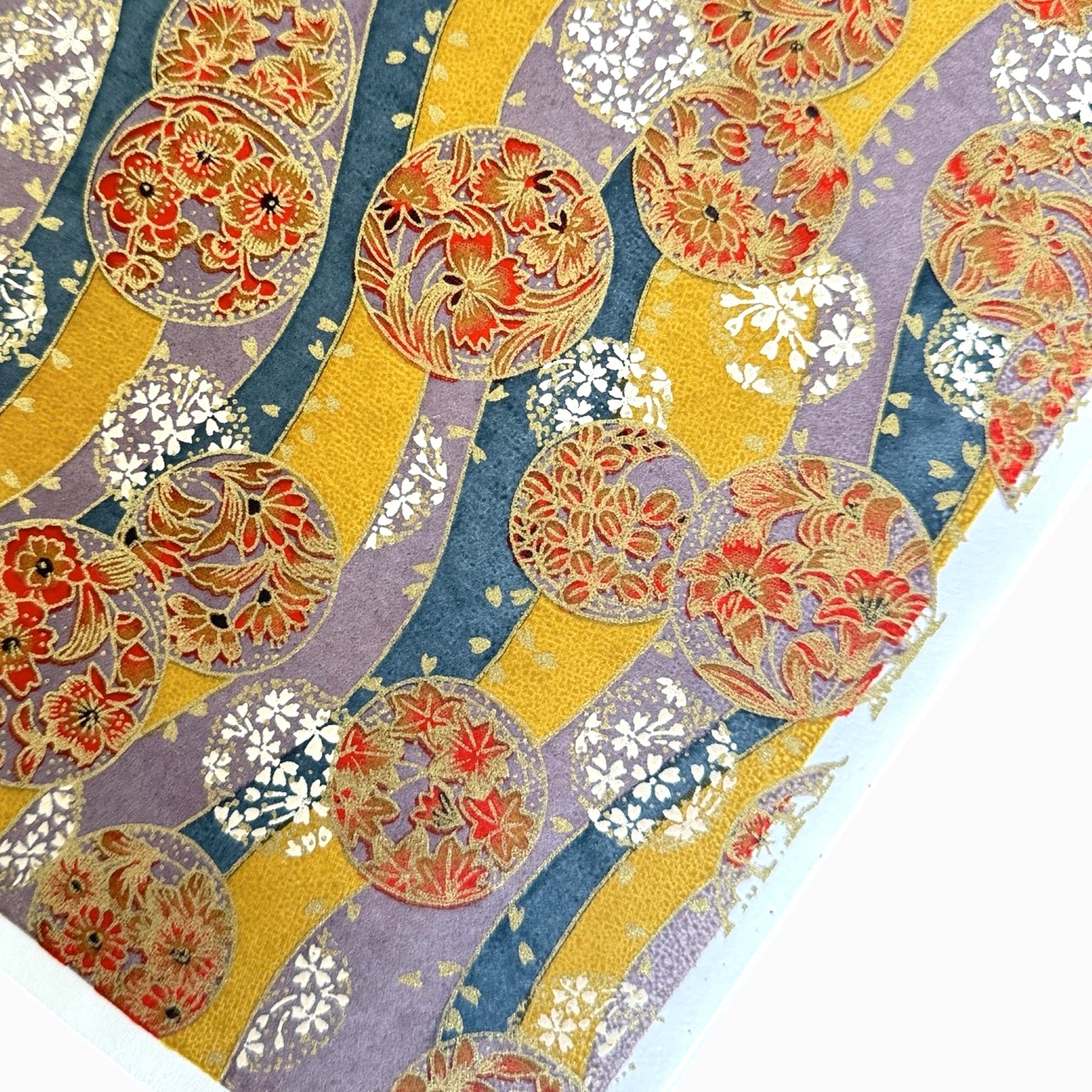 Japanese silkscreen chiyogami paper with a traditional botanical circle motif in tones of mustard, inky blue, lilac and gold.