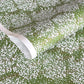 a sheet of japanese chiyogami paper with a grass green background and a dainty pattern of white little flowers with gold