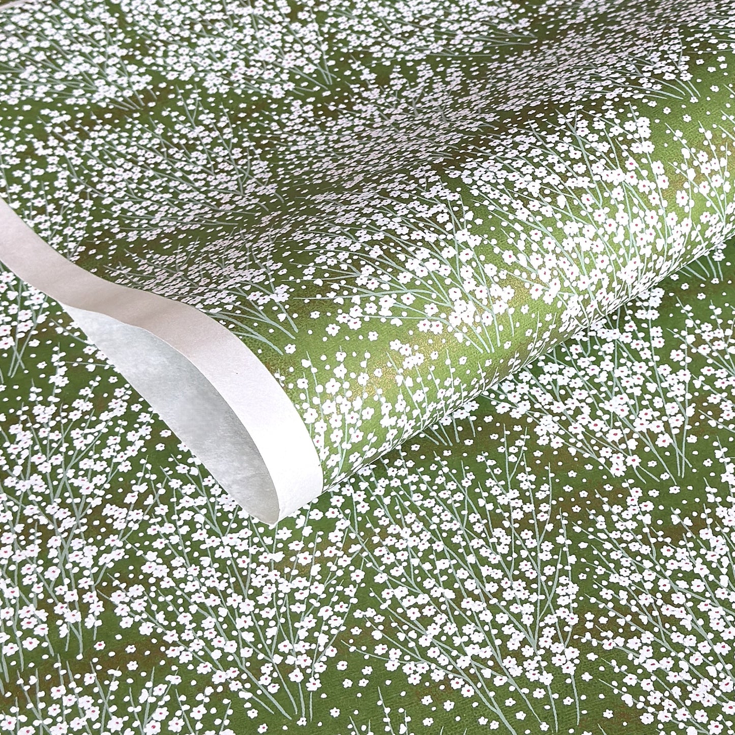a sheet of japanese chiyogami paper with a grass green background and a dainty pattern of white little flowers with gold