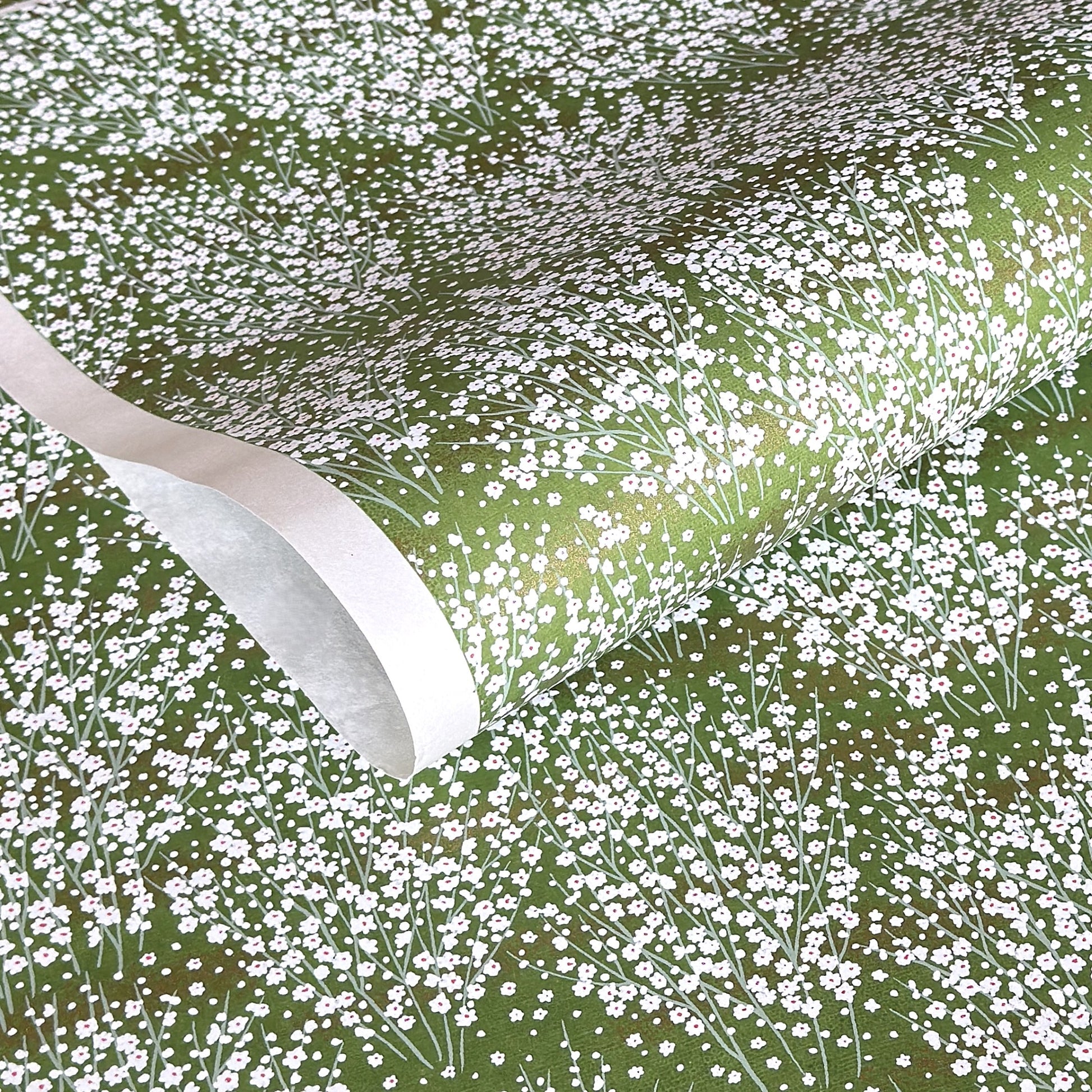 a sheet of japanese chiyogami paper with a grass green background and a dainty pattern of white little flowers with gold
