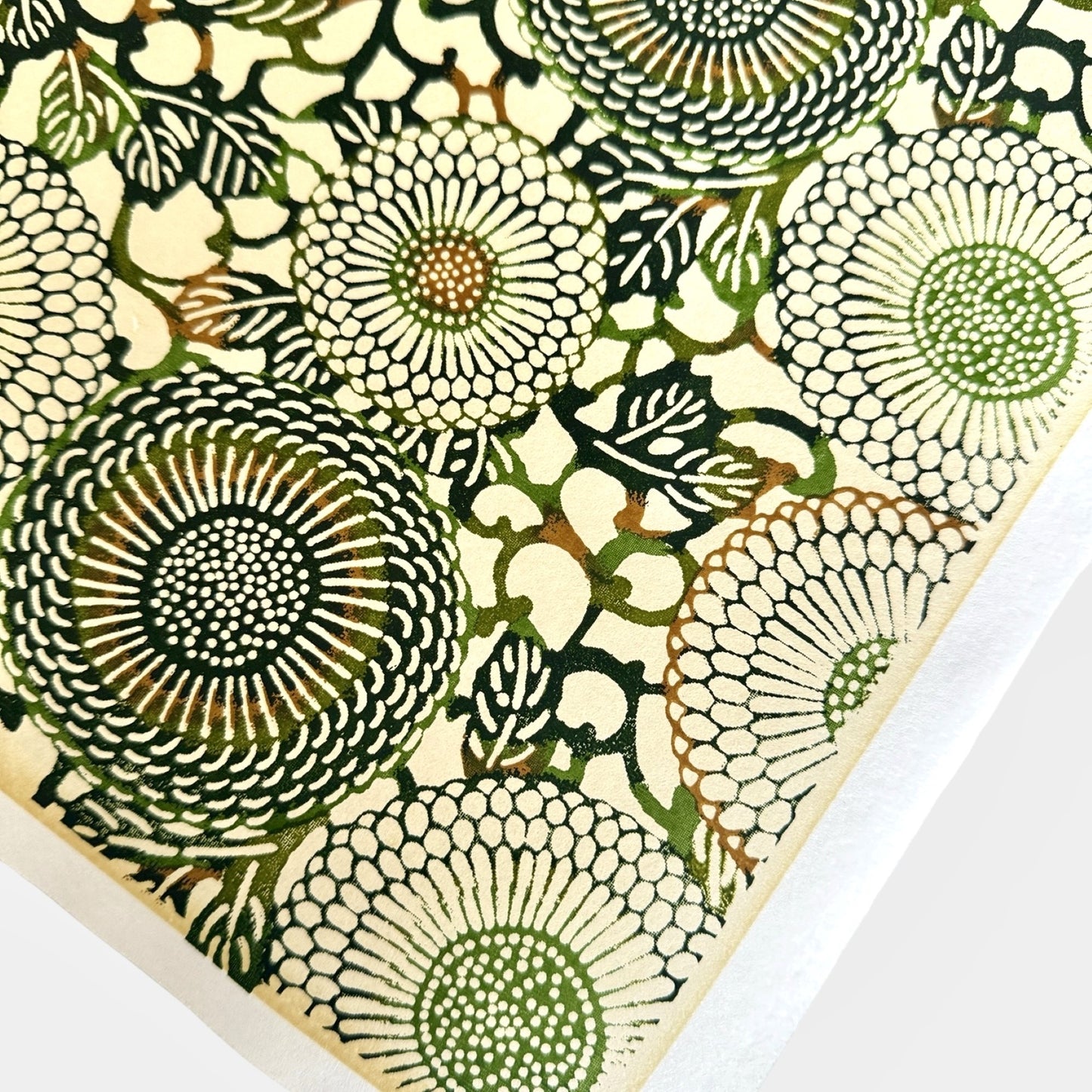 Japanese silkscreen chiyogami paper with a repeat pattern of stylised chrysanthemum flowers in tones of deep green on a buttermilk cream backdrop. Close-up