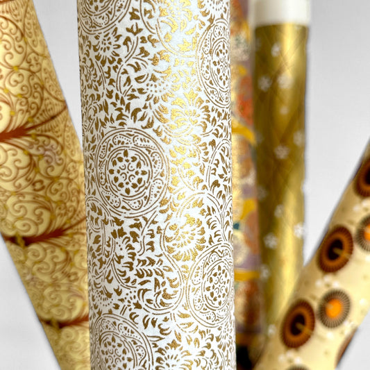 Japanese silkscreen chiyogami paper with an intricate floral pattern in gold on ivory white. Pictured rolled