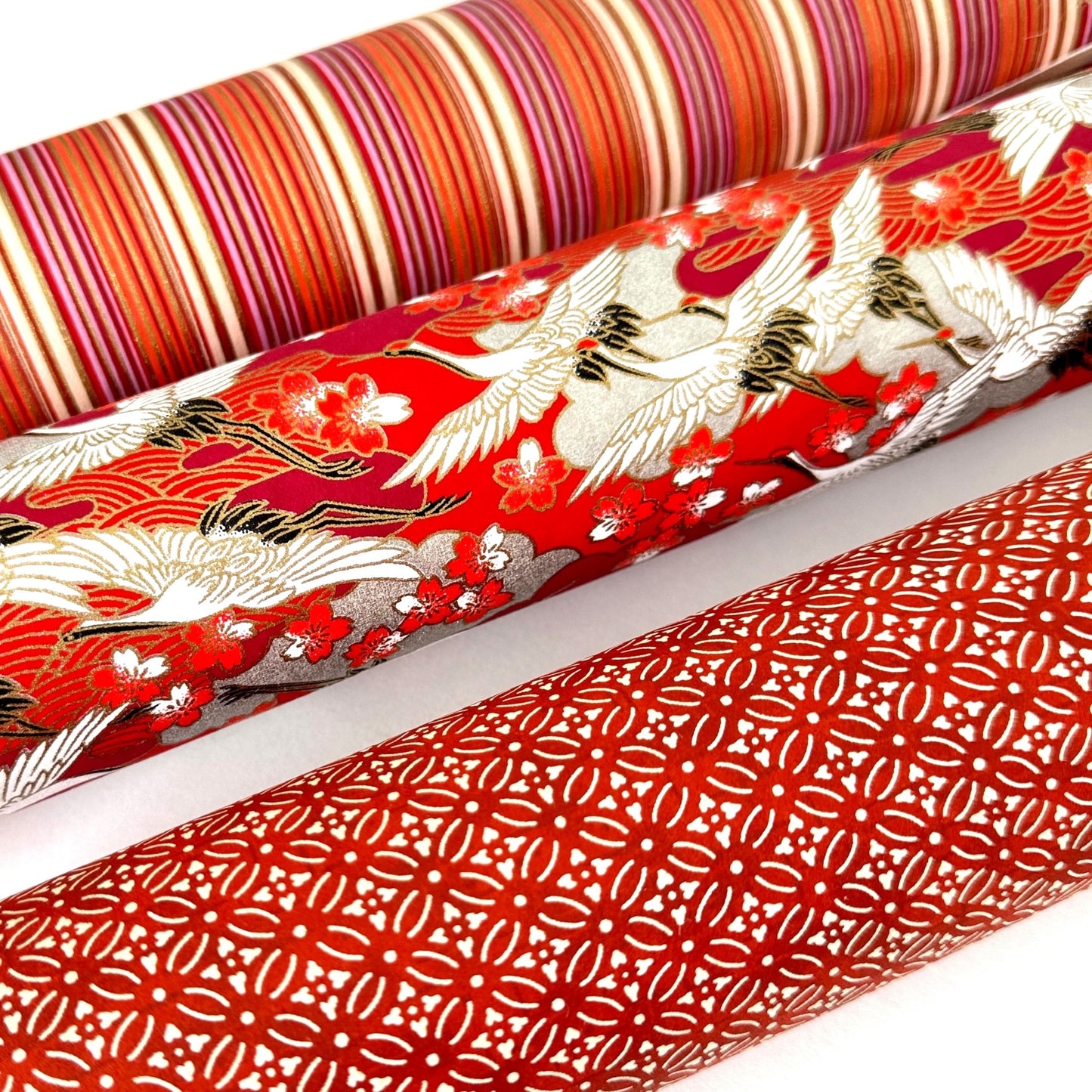Japanese silkscreen chiyogami paper with a two-tone rich red geometric pattern on creamy white. Pictured rolled with other designs
