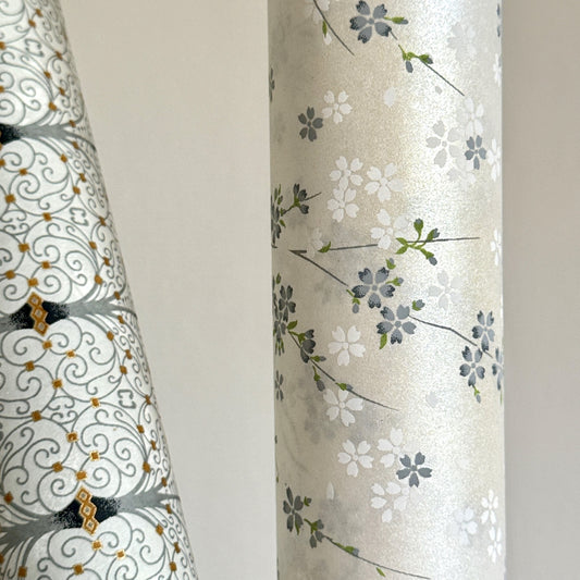 Japanese silkscreen chiyogami paper with a delicate flower design in soft grey on an ivory pearlescent backdrop. Pictured rolled