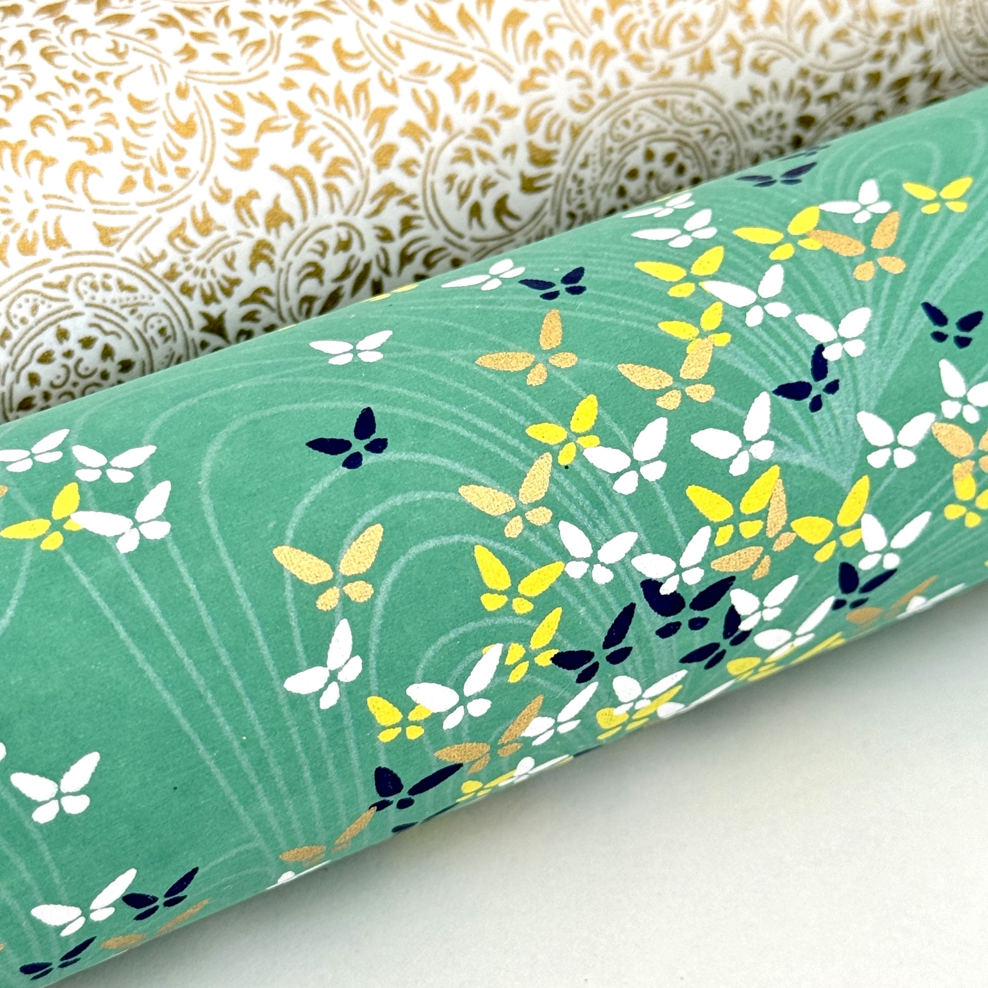 Japanese silkscreen chiyogami paper with a delicate butterfly pattern on a teal backdrop. Close up