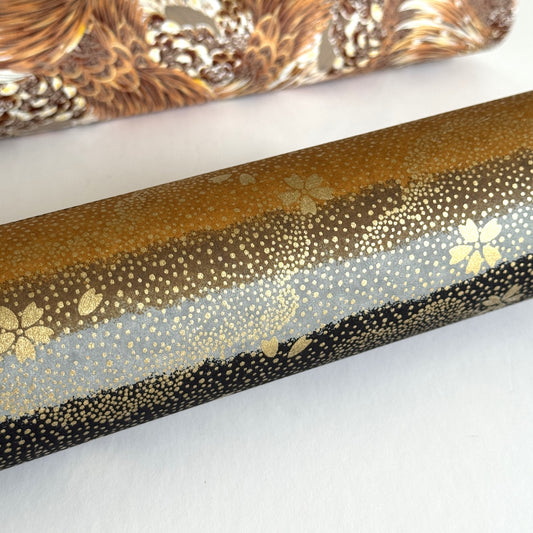 japanese chiyogami paper in stripes of black, brown, ochre and grey with gold clouds and flowers. Close up. rolled