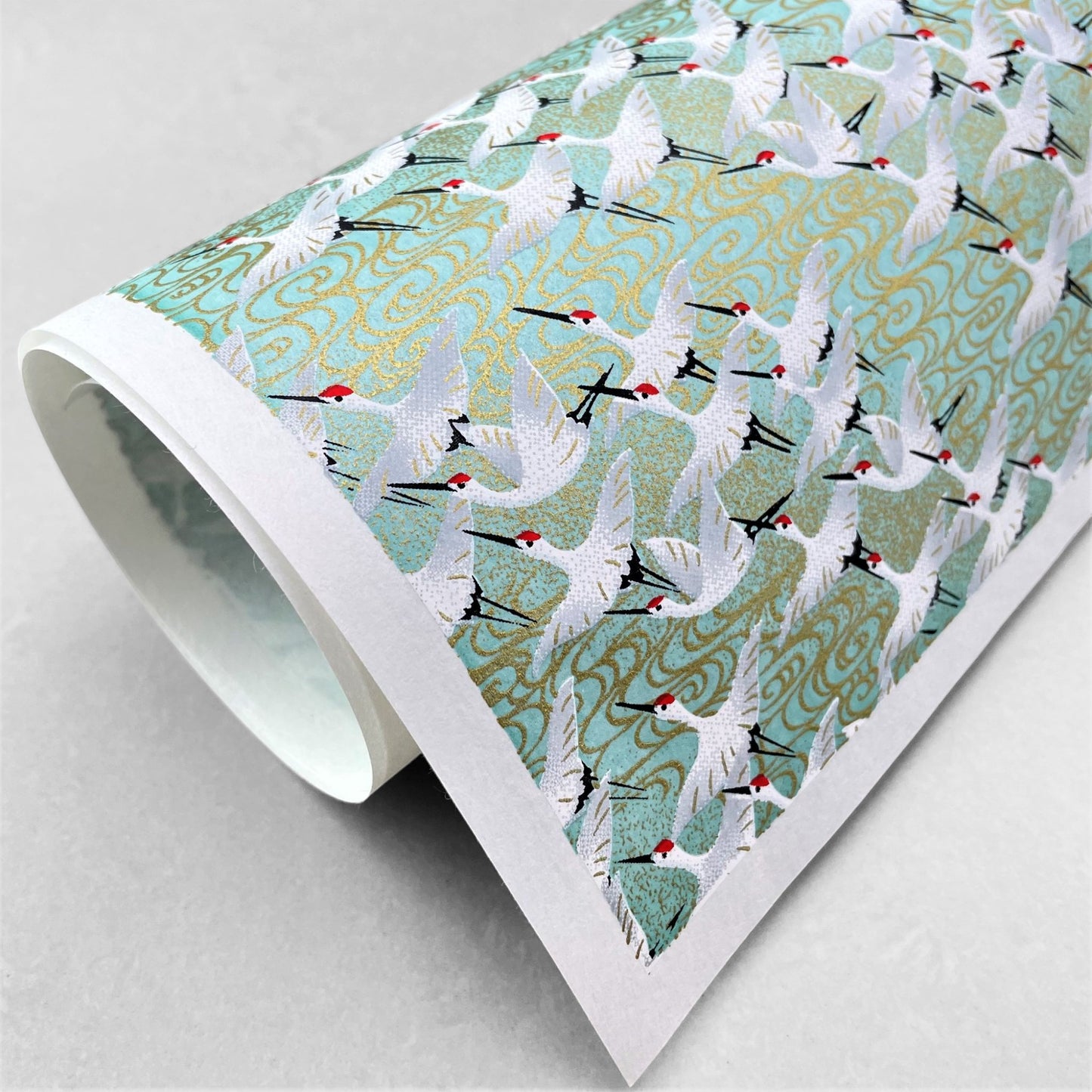 japanese silk-screen handmade paper showing white cranes in flight on a light teal and gold backdrop