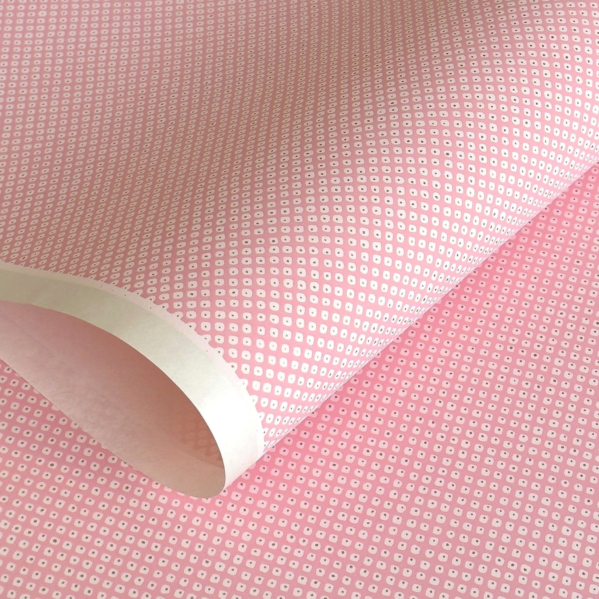 a sheet of chiyogami paper with a pink background and little irregular white dots with a gold center