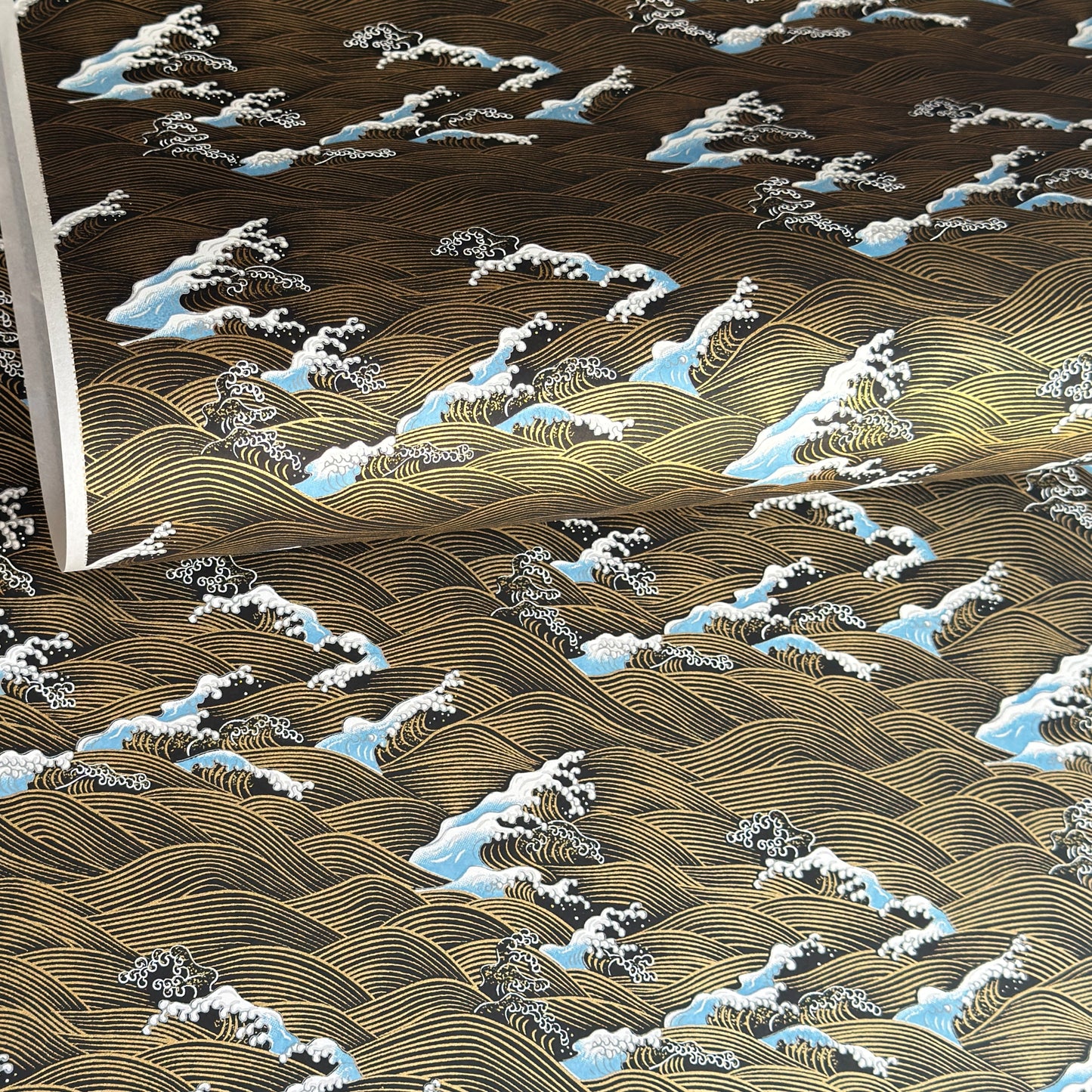 a sheet of Japanese silkscreen printed chiyogami paper with a depiction of pale blue stormy waves in a sea in black and gold