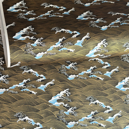 a sheet of Japanese silkscreen printed chiyogami paper with a depiction of pale blue stormy waves in a sea in black and gold