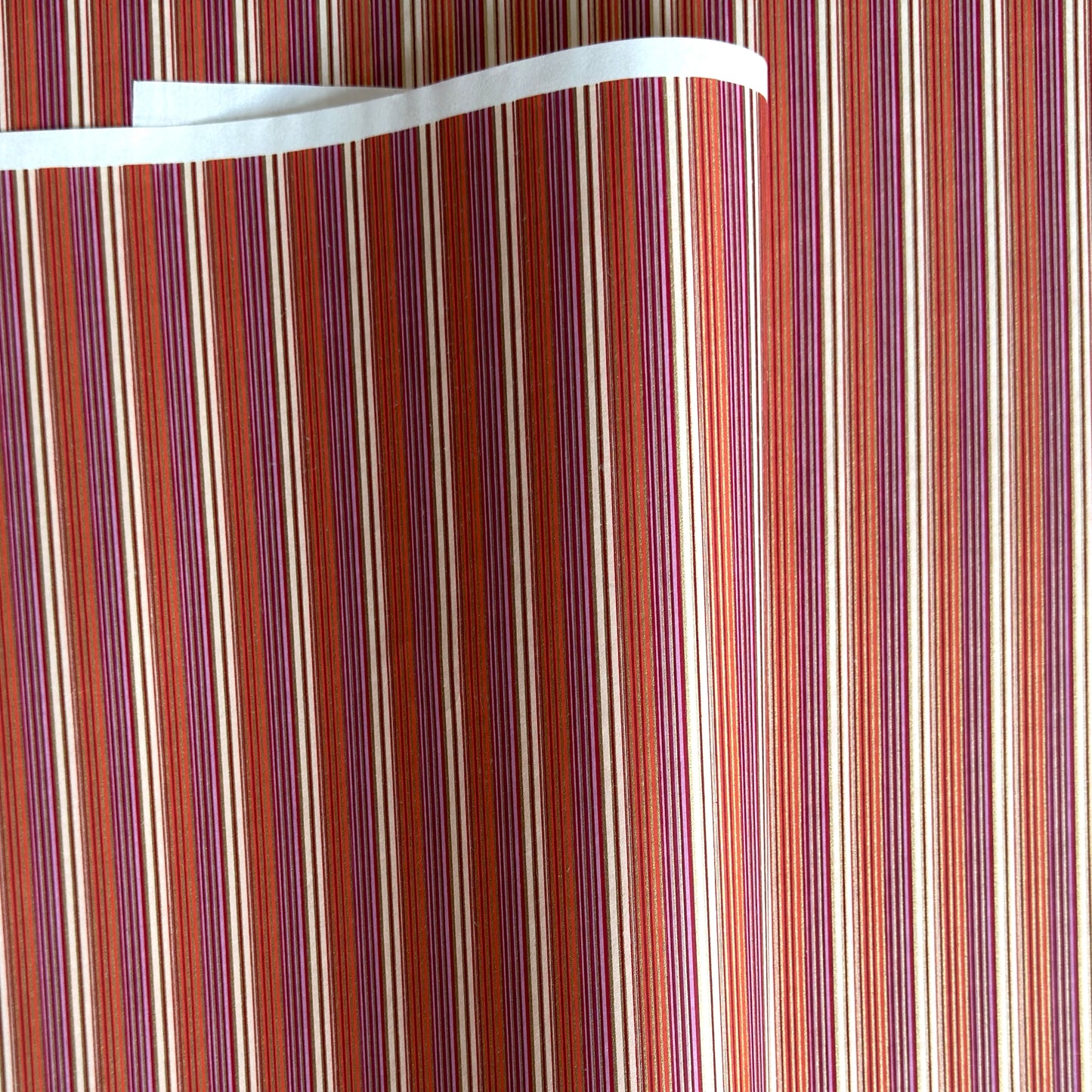 Japanese silkscreen chiyogami paper with a classic narrow stripe pattern in berry tones of red, pink, purple and gold.