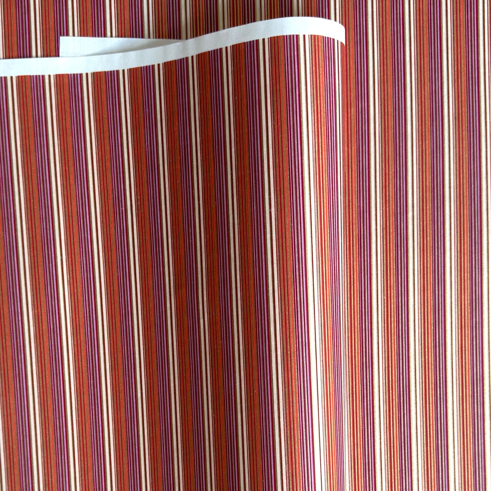 Japanese silkscreen chiyogami paper with a classic narrow stripe pattern in berry tones of red, pink, purple and gold.