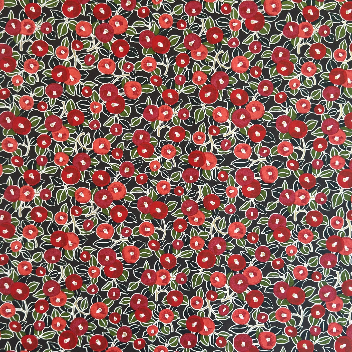 japanese silk-screen handmade paper, chiyogami, with a design showing red and pink camellia flowers and green leaves on black background